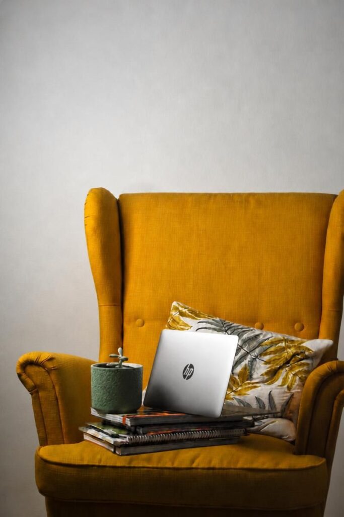 Fauteuil avec une pile de livres et carnets, un ordinateur portable et une petite plante verte